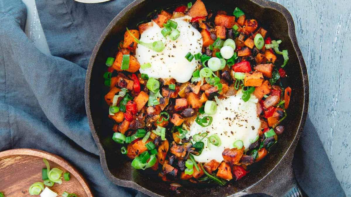 Sweet potato hash with poached eggs in a cast iron skillet.
