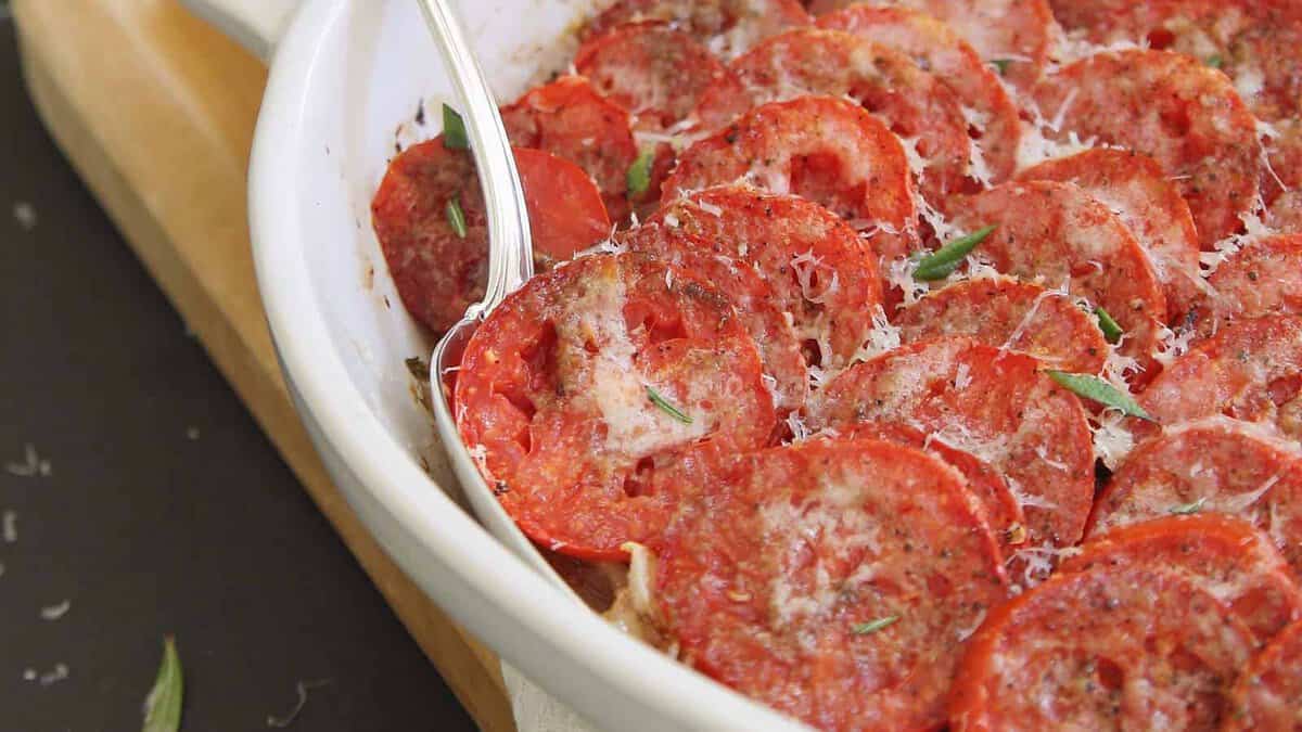 Tomato gratin in a white baking dish with serving spoon.