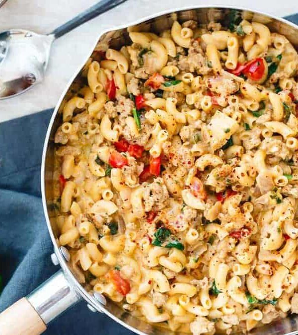 A skillet full of mac and cheese with turkey and herbs.