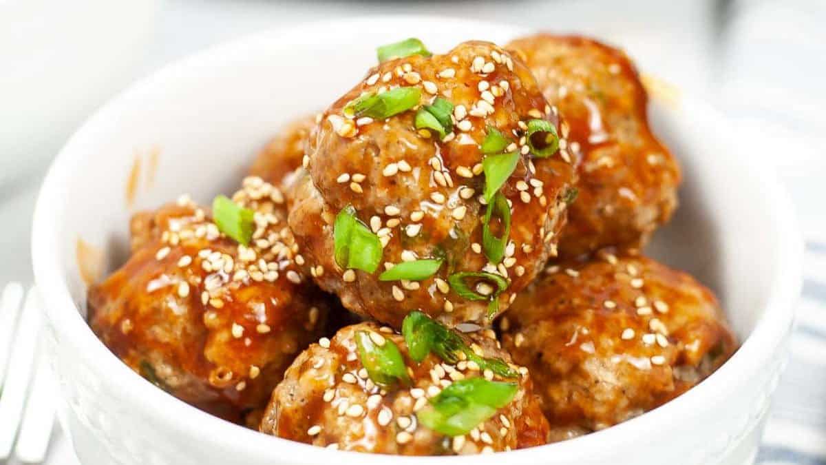 Asian meatballs in a white bowl with sesame seeds.