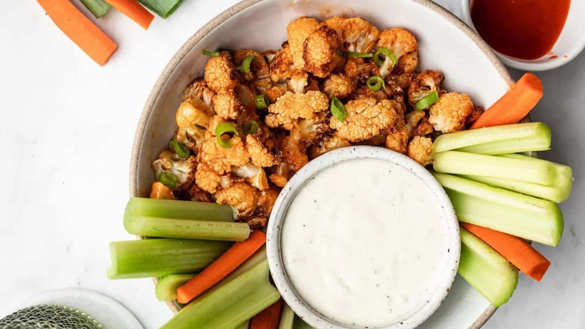 Buffalo cauliflower bites on a plate with celery sticks and carrot sticks and dip.