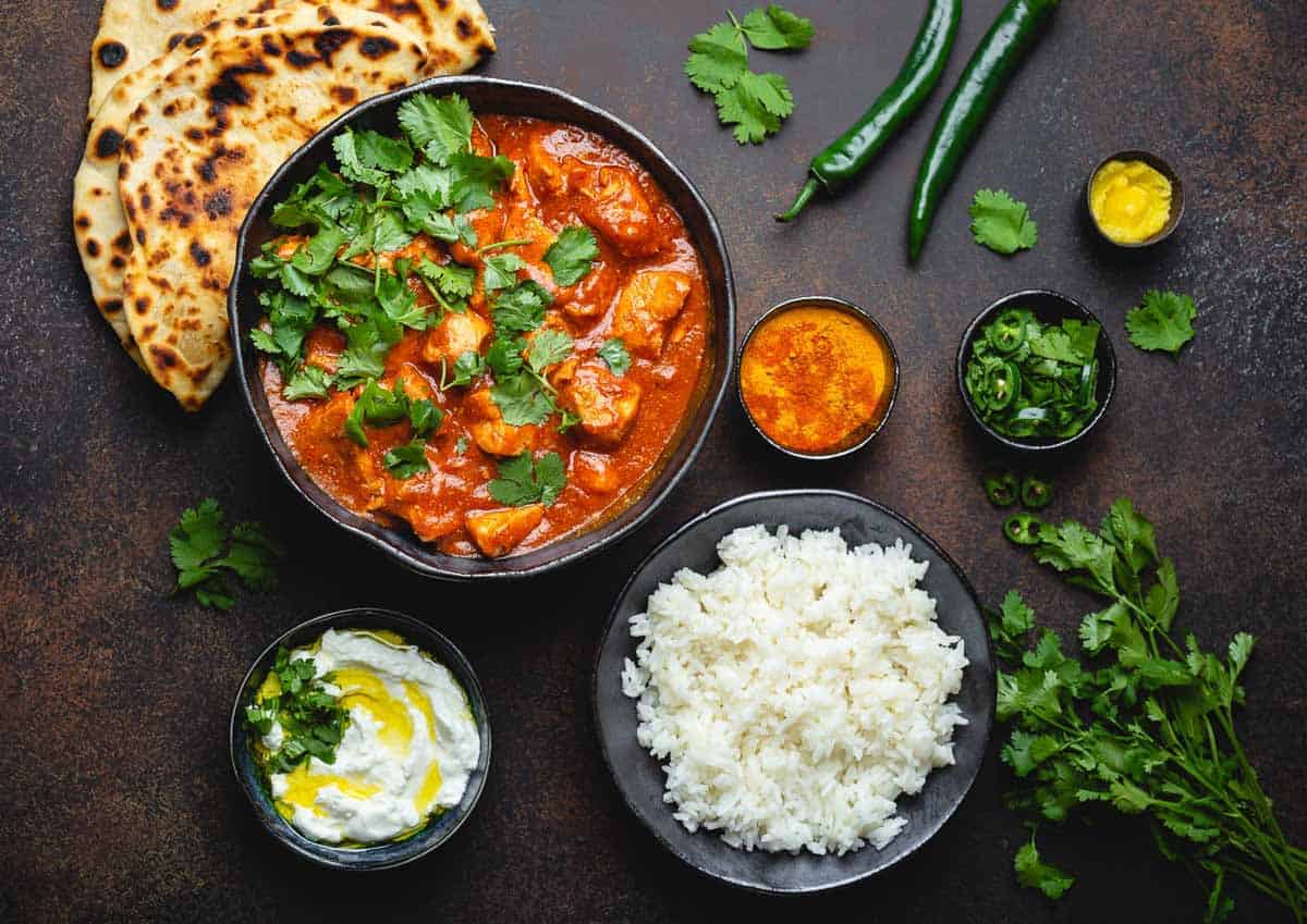 Chicken tikka masala in a black bowl with naan and white rice.