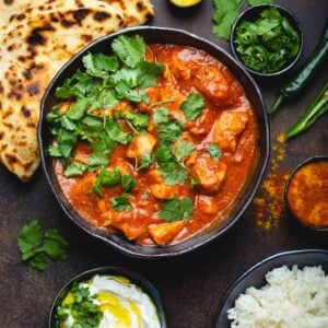 Chicken tikka masala recipe with bowls of rice, yogurt sauce, cilantro, jalapenos and spices.