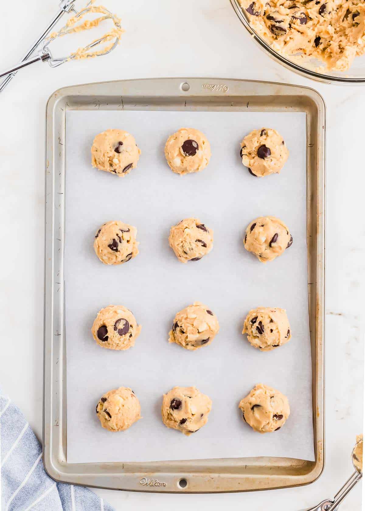 Scoops of macadamia nut chocolate chip cookie dough on a parchment lined baking sheet.