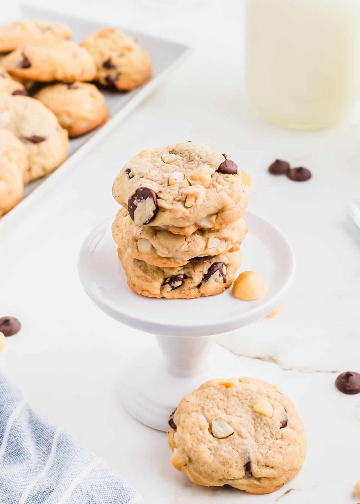 Three cookies on a white cookie stand with chocolate chips and macadamia nuts.