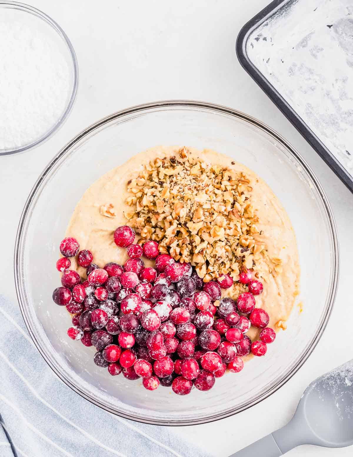 Cranberries and walnuts mixing into batter in a large glass bowl.