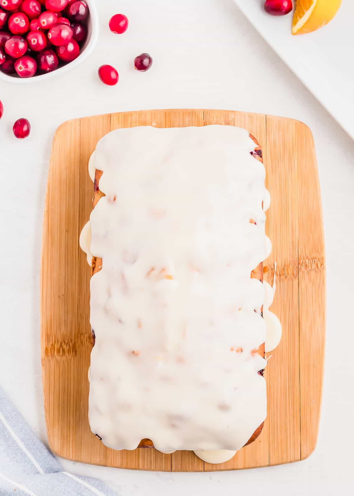 Cranberry orange walnut bread with glaze on a wooden cutting board.