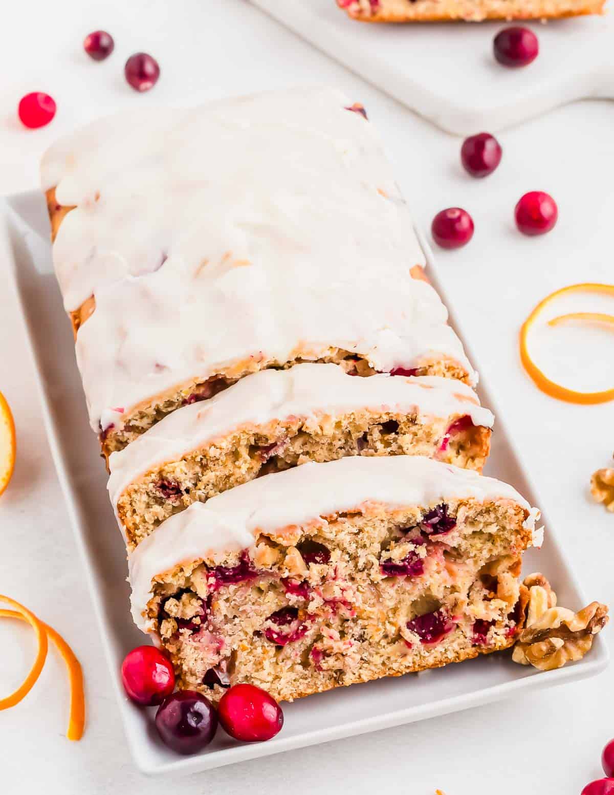Slice orange cranberry bread on a white serving plate with cranberries and orange zest.