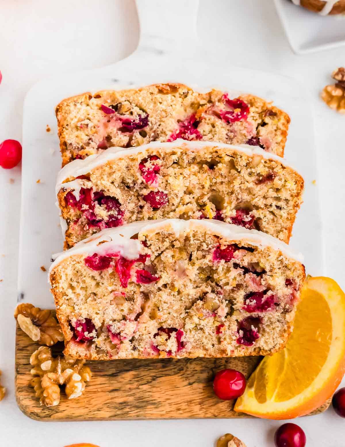 Three slices of glazed orange cranberry bread on cutting board.