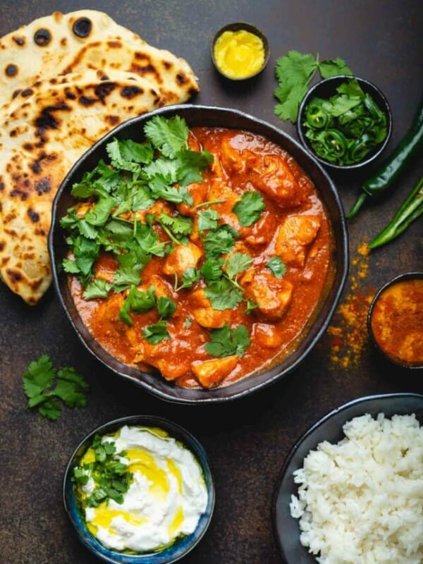Chicken tikka masala recipe with bowls of rice, yogurt sauce, cilantro, jalapenos and spices.