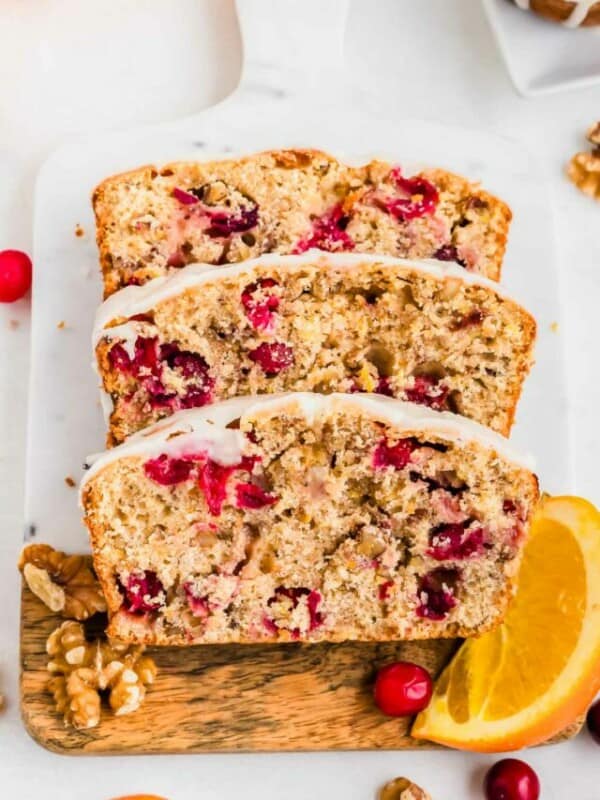 Three slices of glazed orange cranberry bread on cutting board.