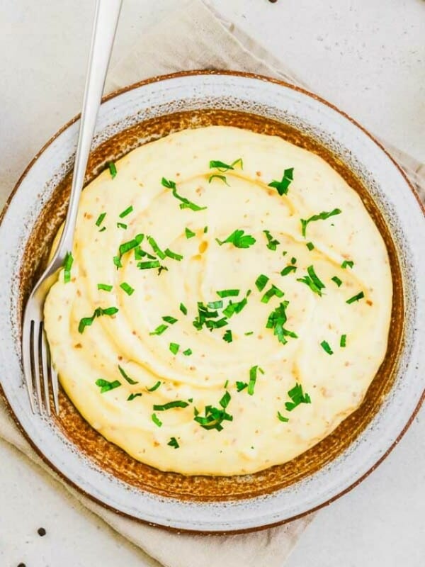 Landscape photo of mashed potatoes with parsley and peppercorns scattered about.