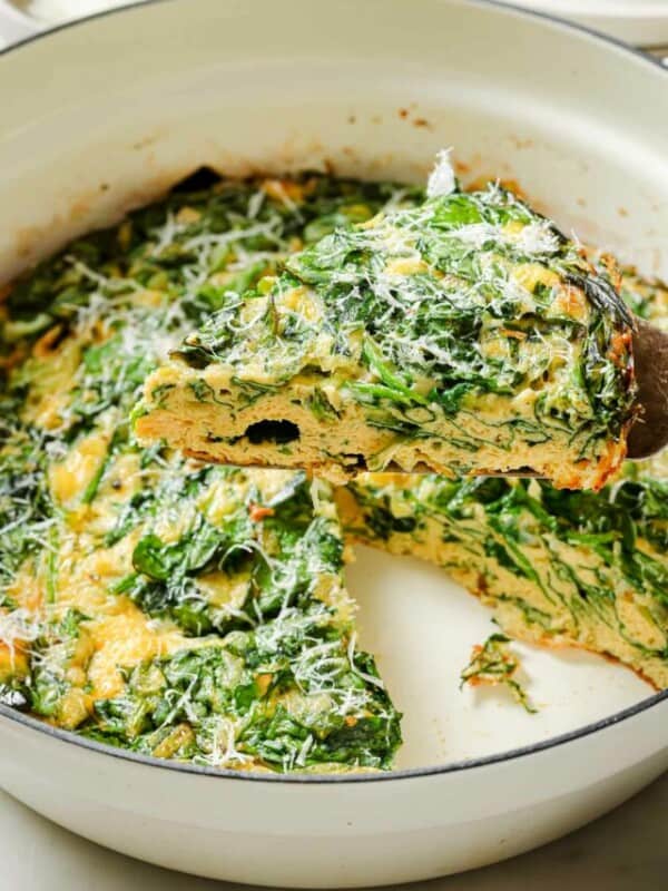 Spinach frittata on a wooden serving utensil being lifted out of a baking dish.