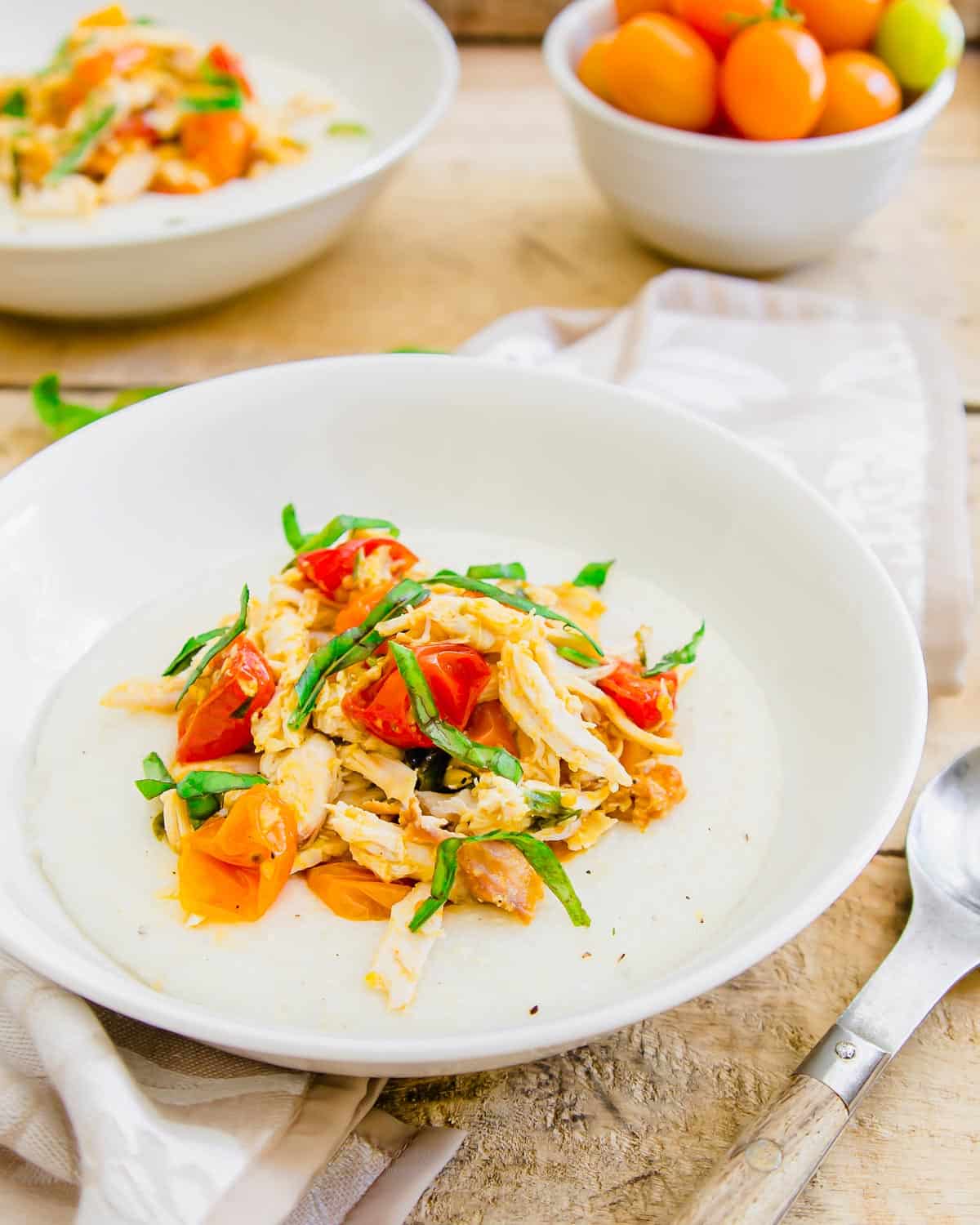 Goat cheese grits topped with chicken and tomatoes in a white bowl.