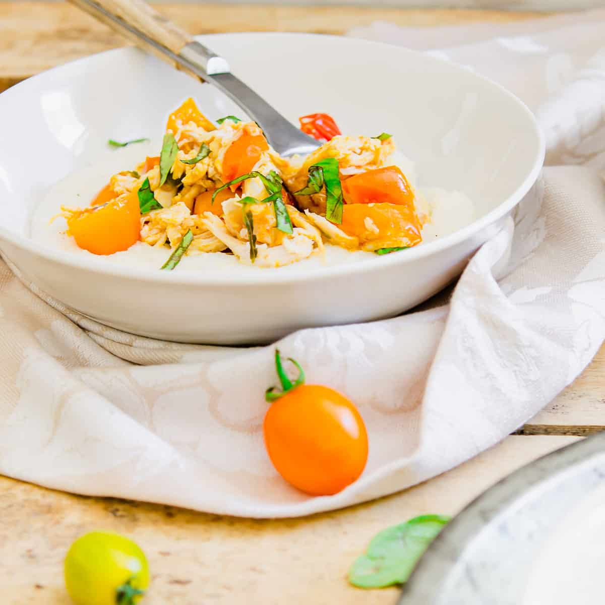 A spoon in a bowl of goat cheese grits with chicken and tomatoes.