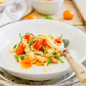 Wooden spoon in a white bowl with creamy grits, goat cheese, chicken and burst tomatoes.