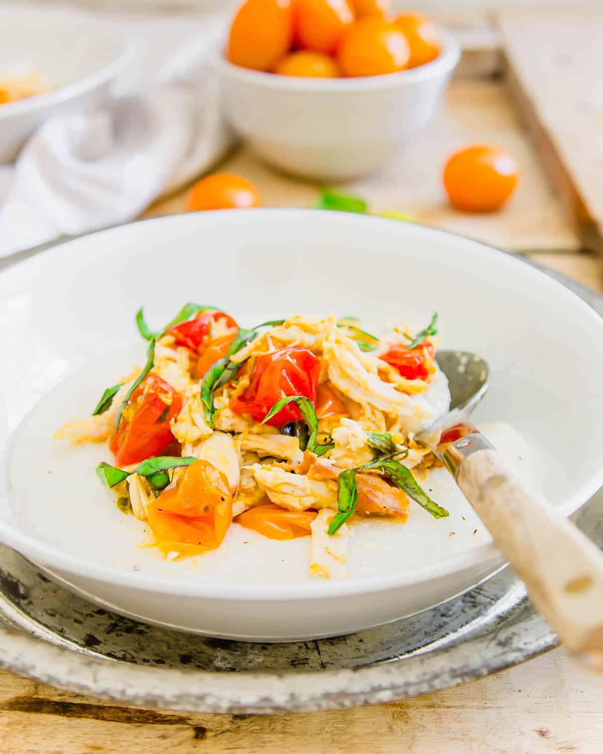 Wooden spoon in a white bowl with creamy grits, goat cheese, chicken and burst tomatoes.