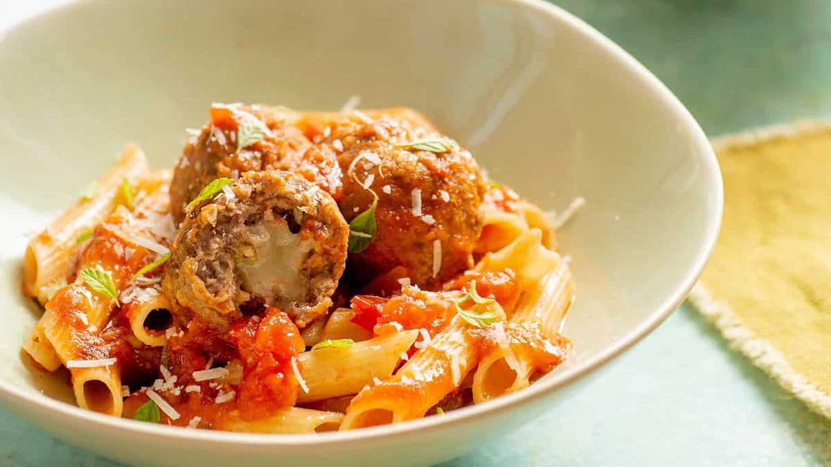 A bowl of pasta with meatballs and sauce.