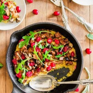 Overhead picture of a cast iron skillet with polenta topped with sausage, mushrooms and cranberries.