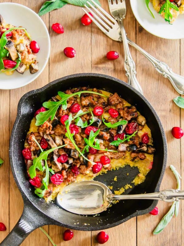 Overhead picture of a cast iron skillet with polenta topped with sausage, mushrooms and cranberries.