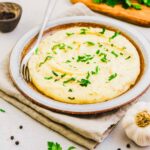 Mashed red skin potatoes in a serving bowl garnished with parsley and a fork on the side.
