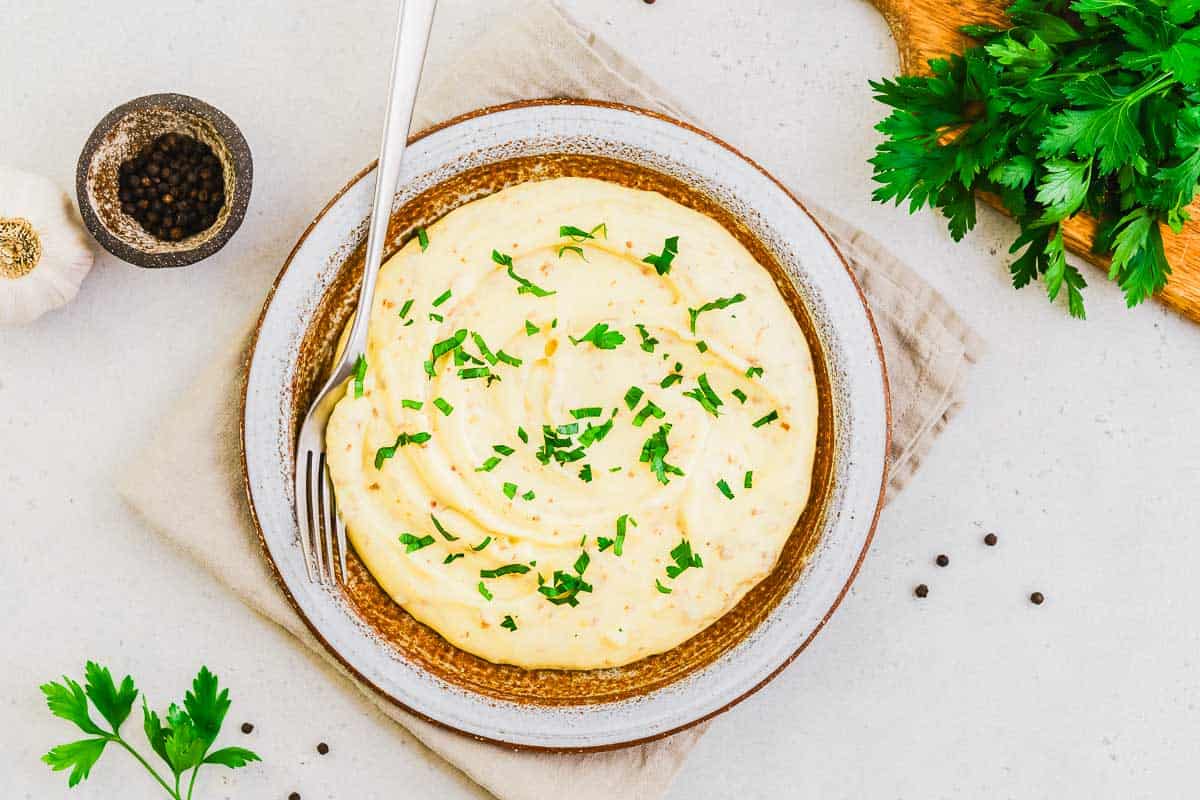 Landscape photo of mashed potatoes with parsley and peppercorns scattered about.