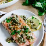 Salmon piccata on a white plate with a lemon slice.
