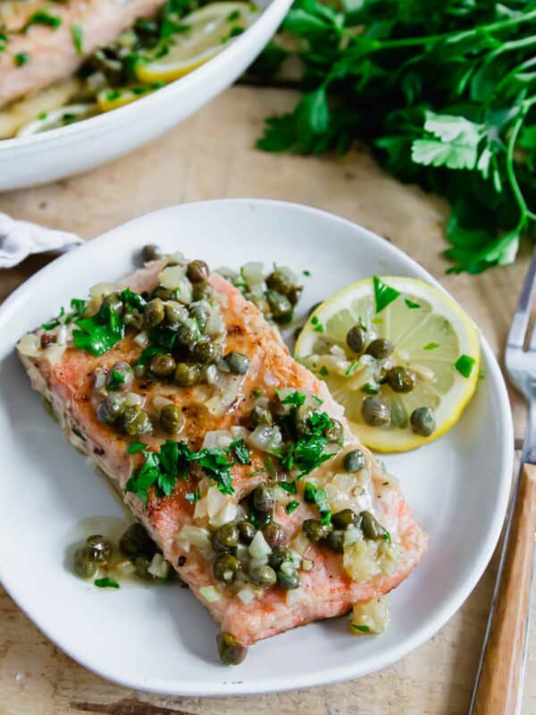 Salmon piccata on a white plate with a lemon slice.