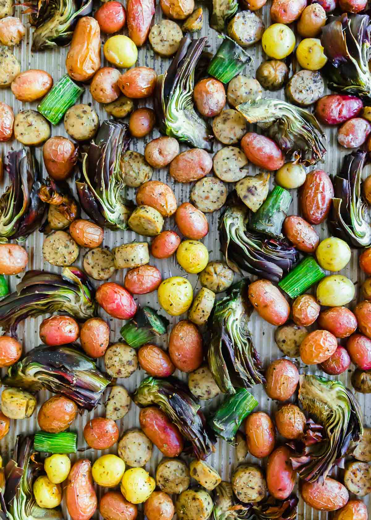 Roasted vegetables and potatoes on a baking sheet with chicken sausage.