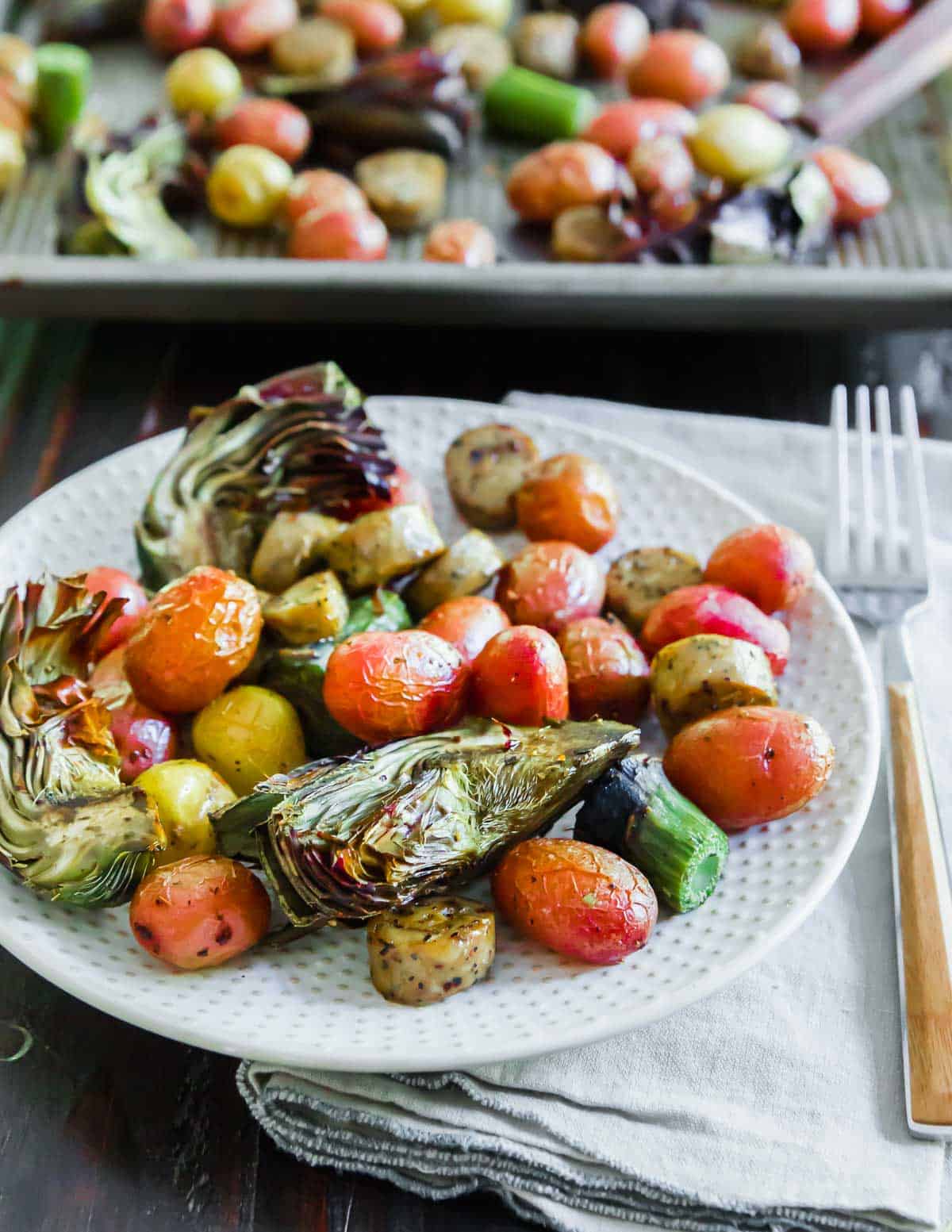Roasted vegetables, artichokes and sausage on a plate with a fork.