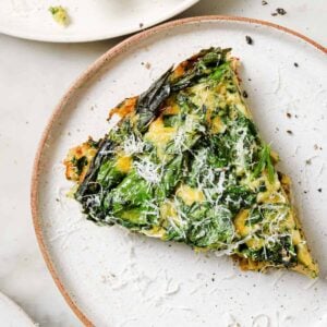 Spinach frittata slice on a white plate topped with grated parmesan cheese.