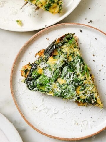 Spinach frittata slice on a white plate topped with grated parmesan cheese.