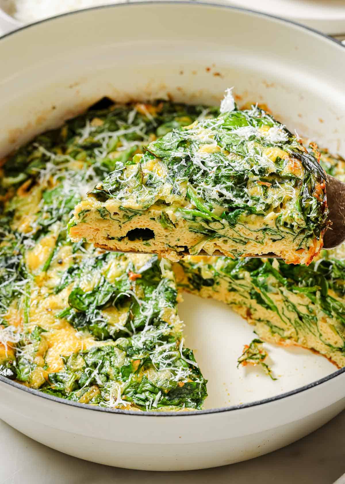 Spinach frittata on a wooden serving utensil being lifted out of a baking dish.