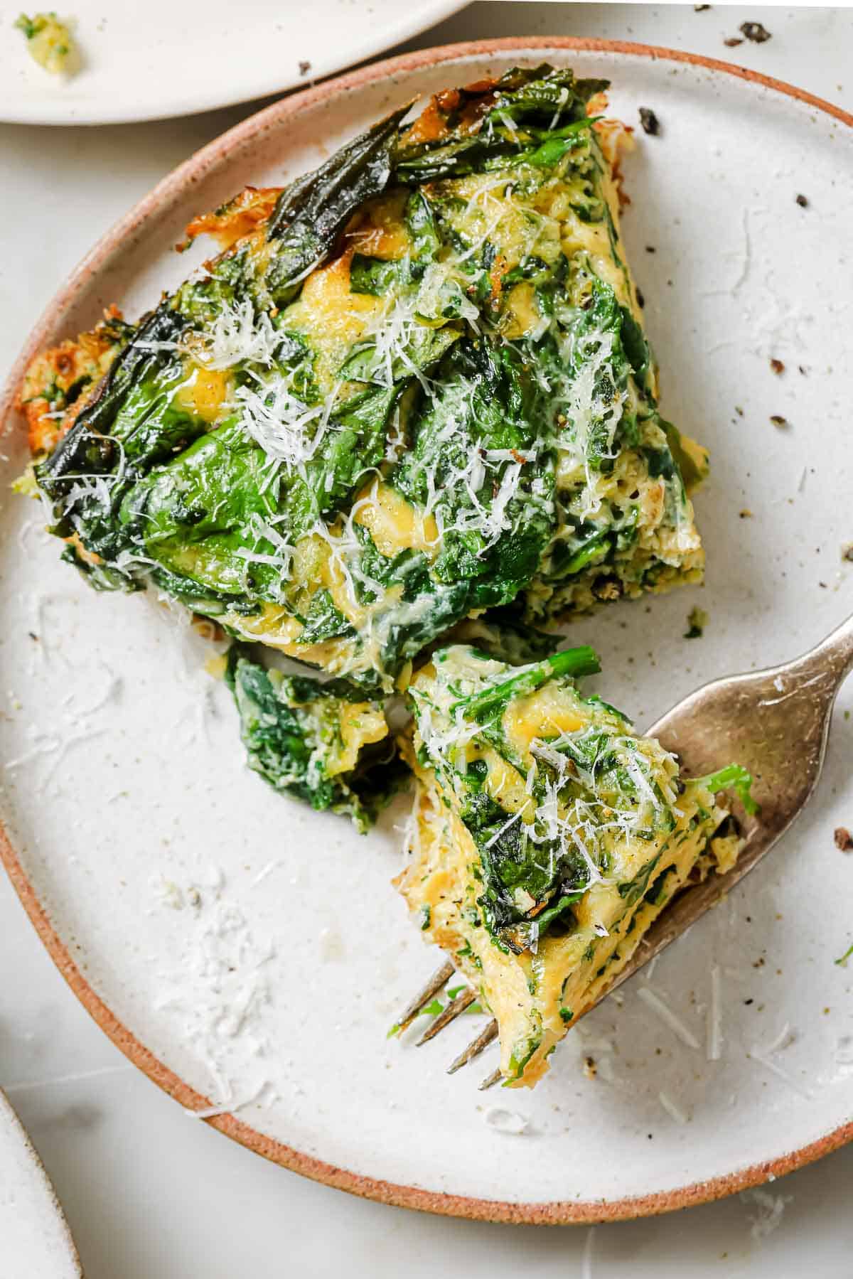 A slice of spinach parmesan frittata on a white plate with a fork.