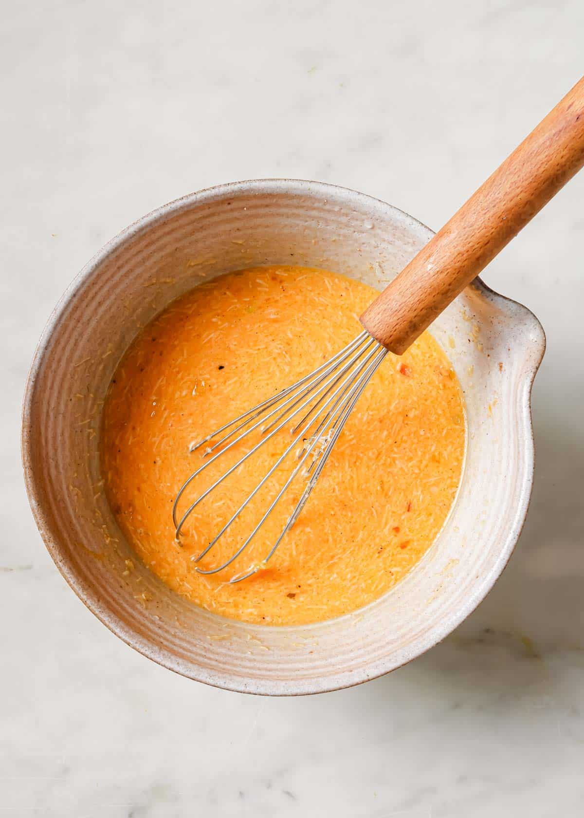 Beaten eggs combined with parmesan cheese in a bowl with a whisk.