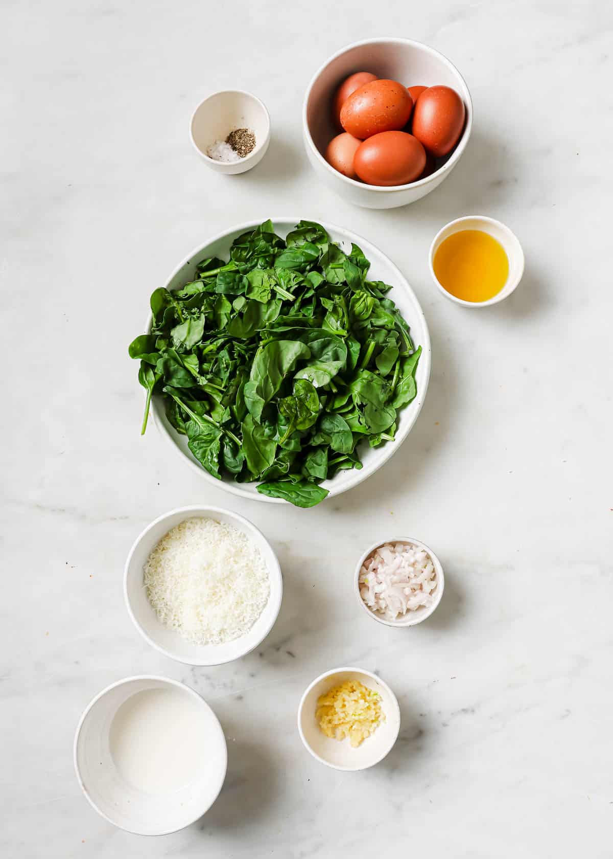 Ingredients to make a spinach frittata in bowls on a white surface.