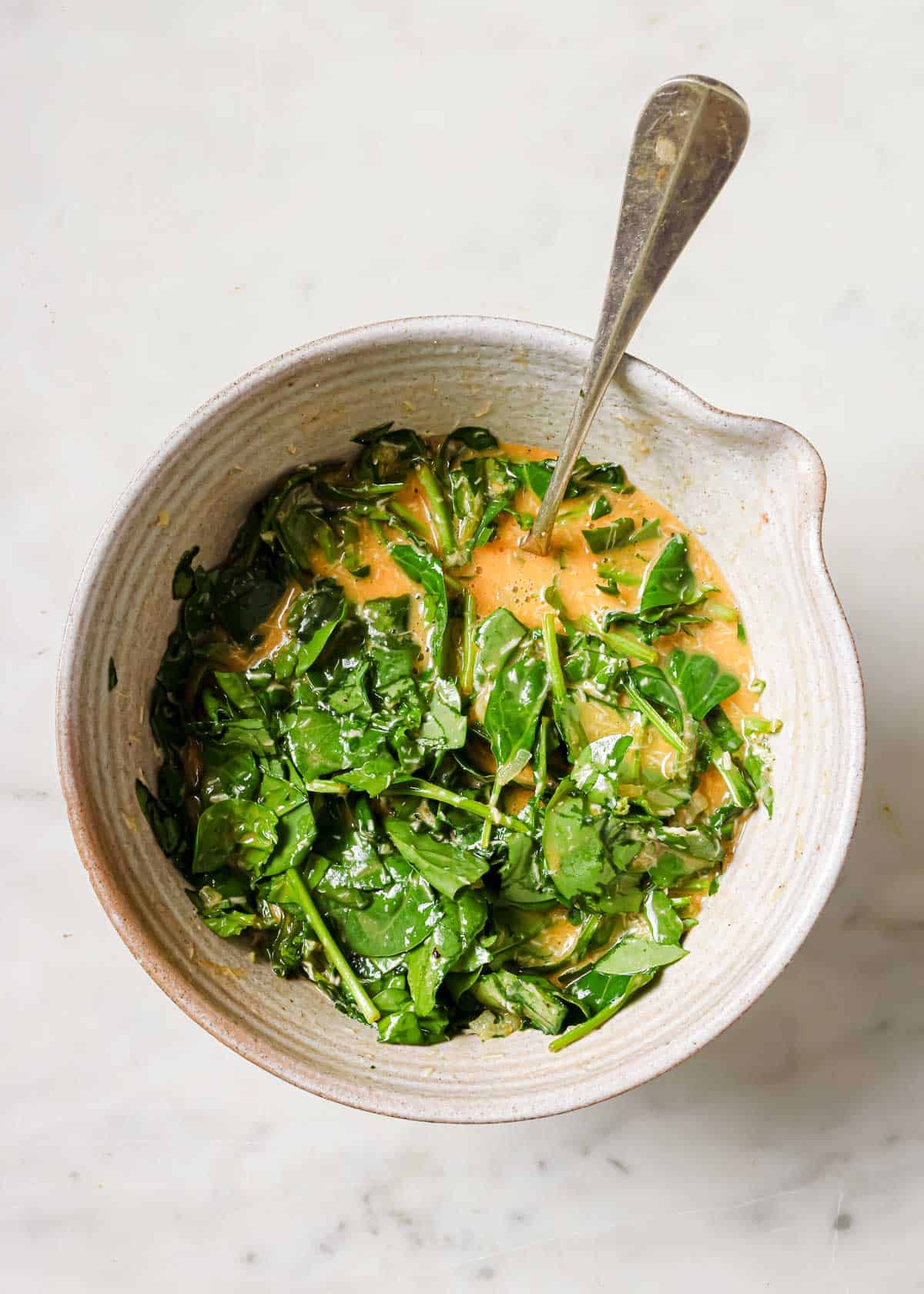 Mixing beaten eggs and baby spinach together in a bowl.