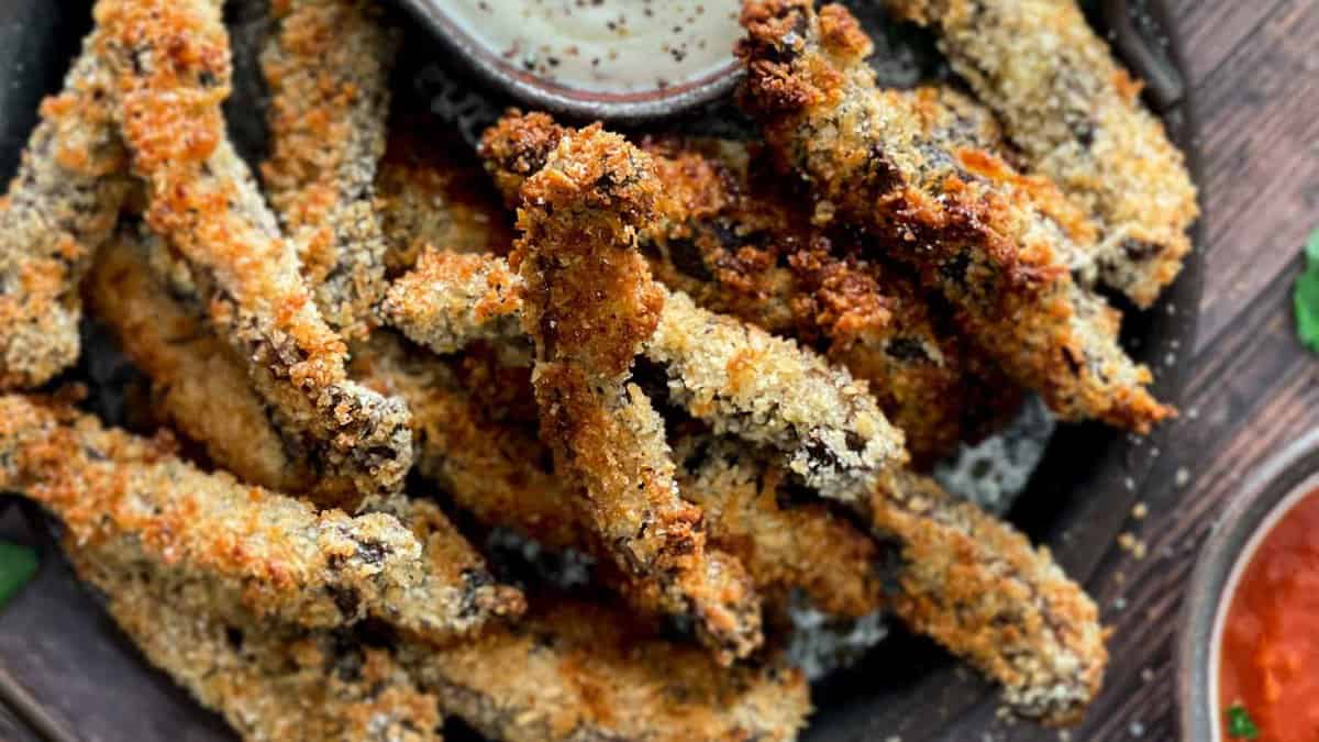 Fried zucchini sticks with dipping sauce on a plate.