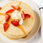 Pancakes with whipped cream and strawberries on a plate.