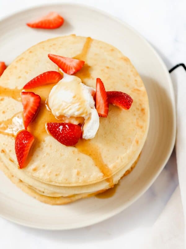 Pancakes with whipped cream and strawberries on a plate.