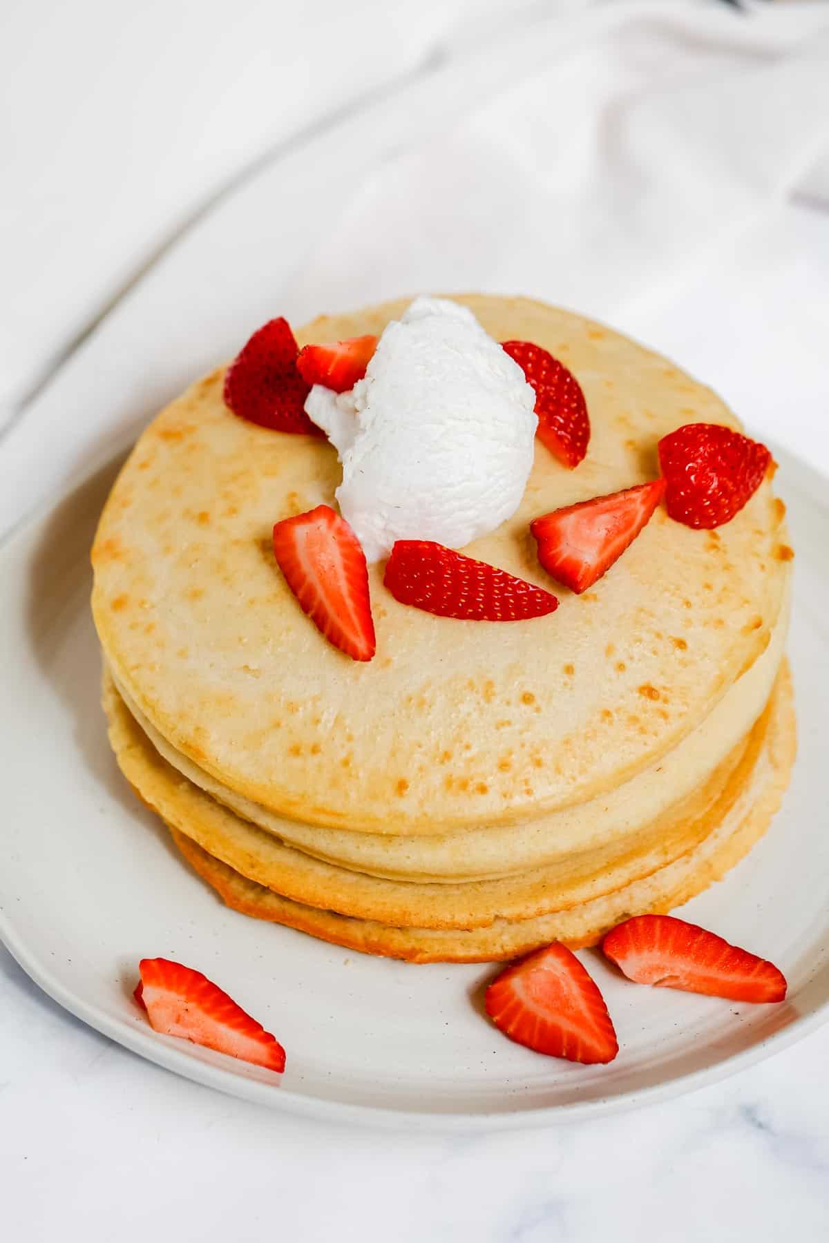 Pancakes topped with strawberries and whipped cream.