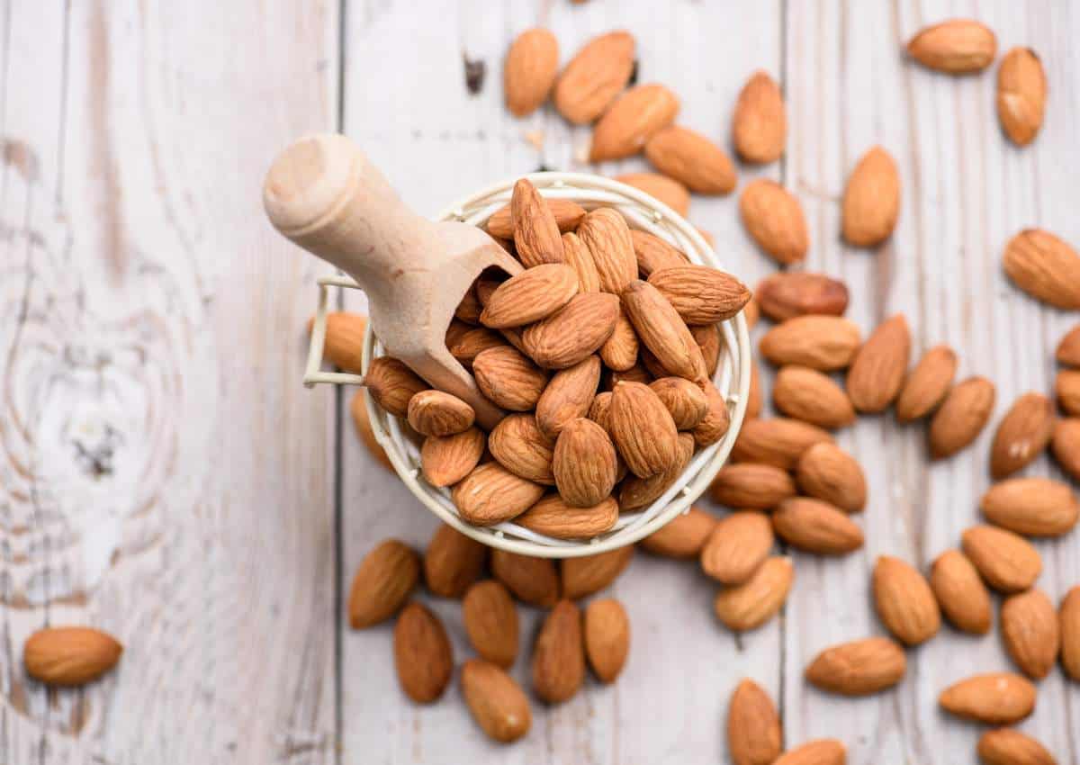 A bucket of almonds with a wooden scoop.