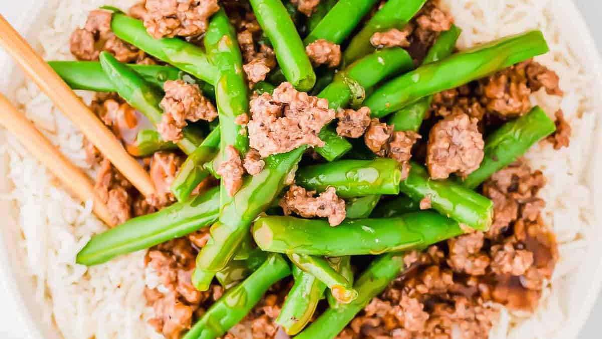A white bowl with green beans and meat on it.
