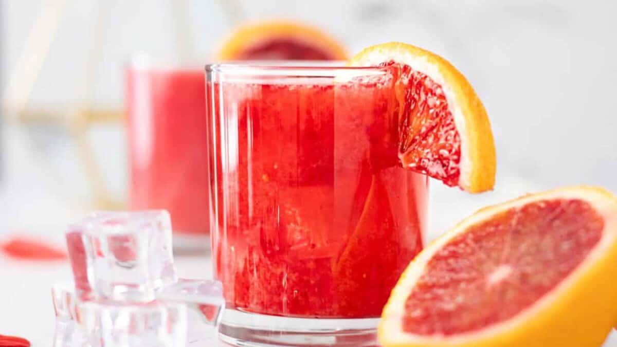 A glass of blood orange juice with a slice of orange.