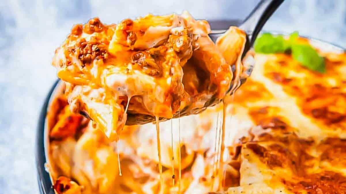 A spoonful of lasagna being taken out of the oven.