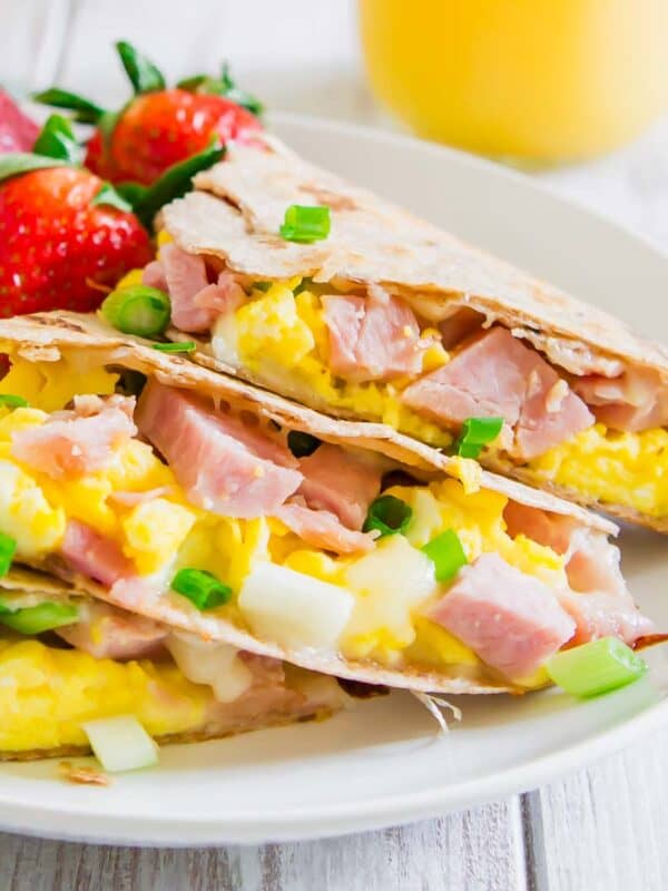 A plate with a ham and egg quesadilla and whole strawberries on it.