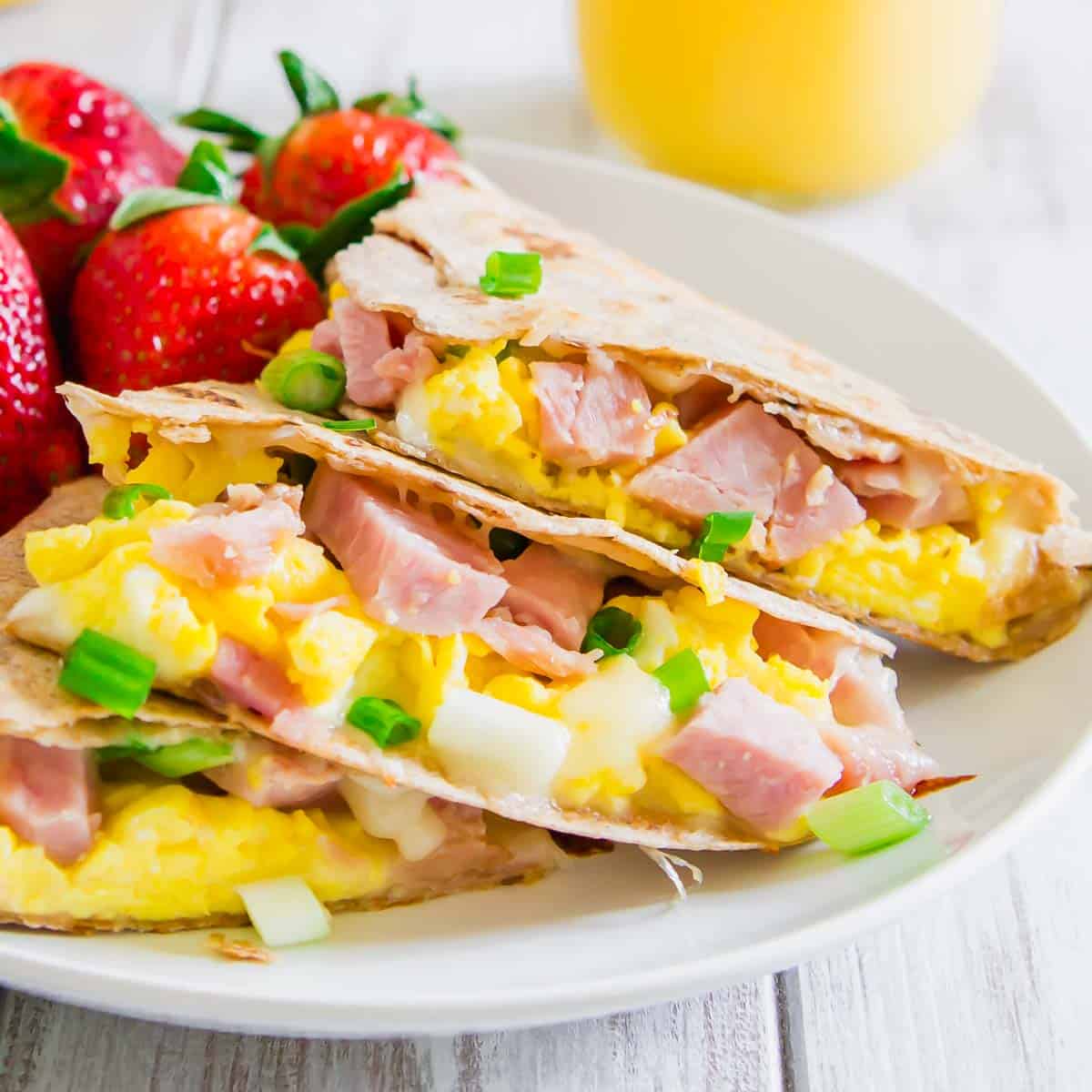 A plate with a ham and egg quesadilla and whole strawberries on it.