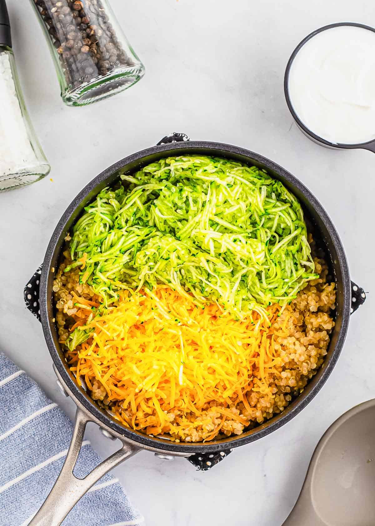 A skillet filled with shredded zucchini, cheese and quinoa.