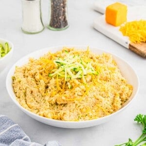 A bowl of cheesy quinoa topped with shredded cheddar cheese and zucchini.