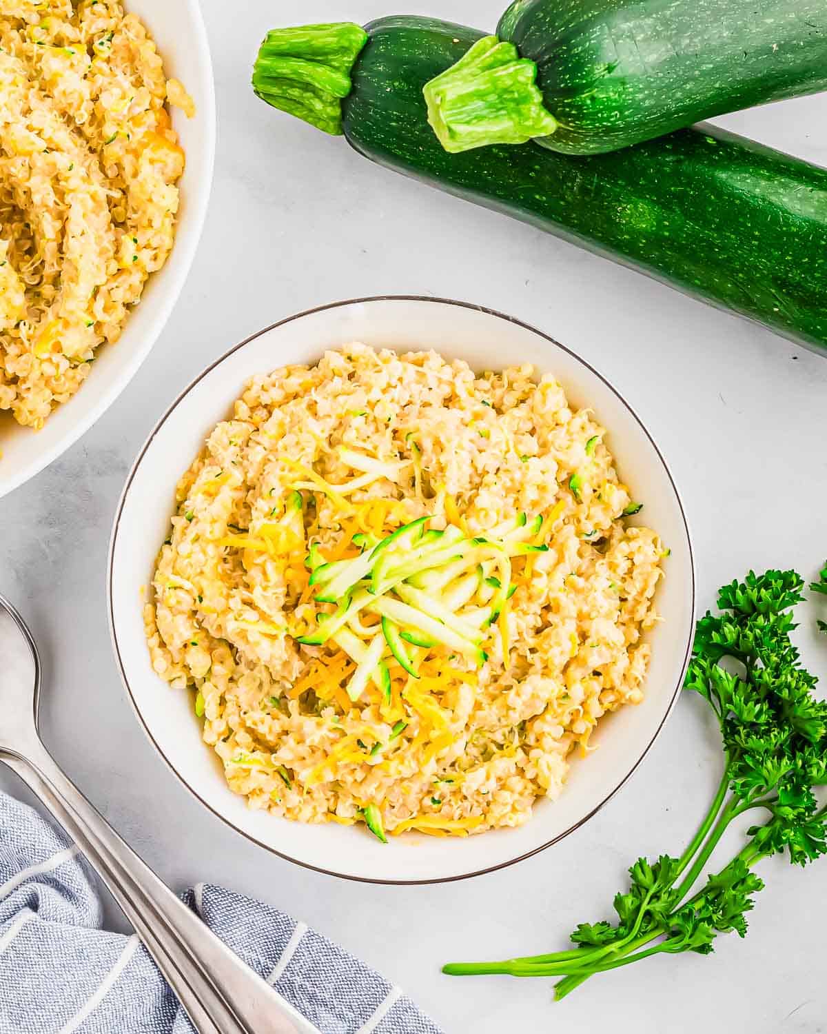 A bowl of a cheesy quinoa recipe garnished with shredded zucchini and cheddar.